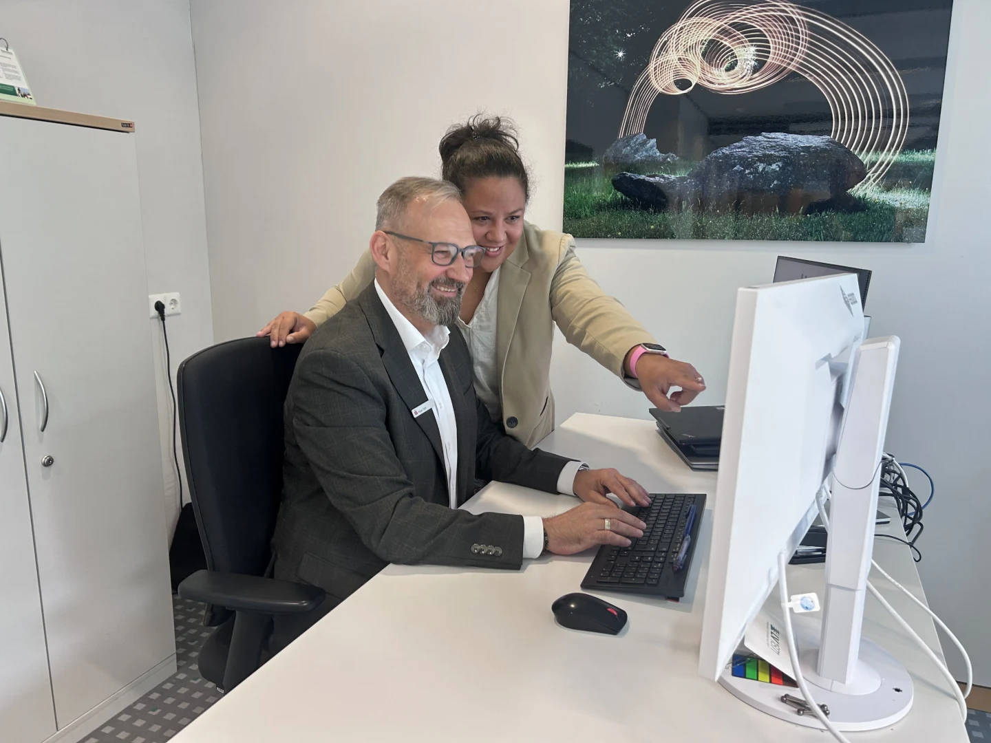 Ein Kollege aus der Versicherungsagentur sitzt im Büro an seinem Schreibtisch, eine weitere Kollegin schaut ihm über die Schulter und sie werten gemeinsam Kundendaten für den nächsten Termin aus.