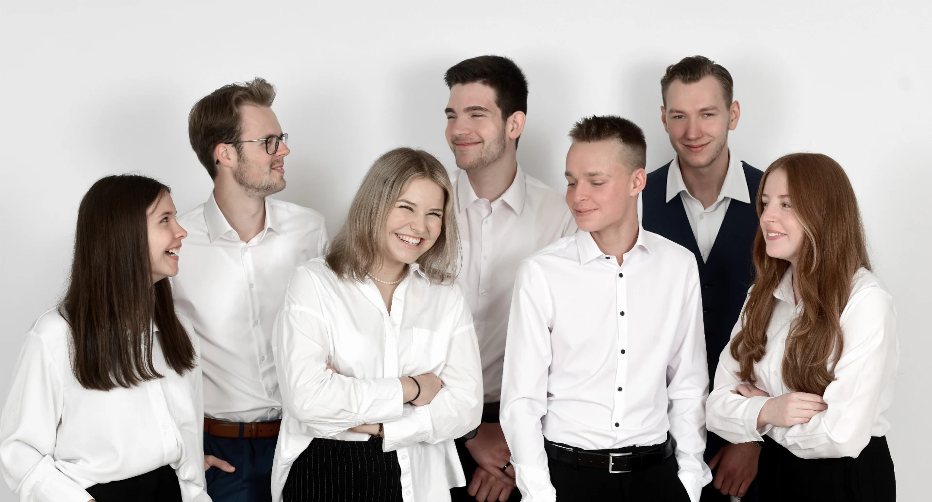 Sieben junge Azubis in weißen Oberteilen posieren für ein Gruppenfoto