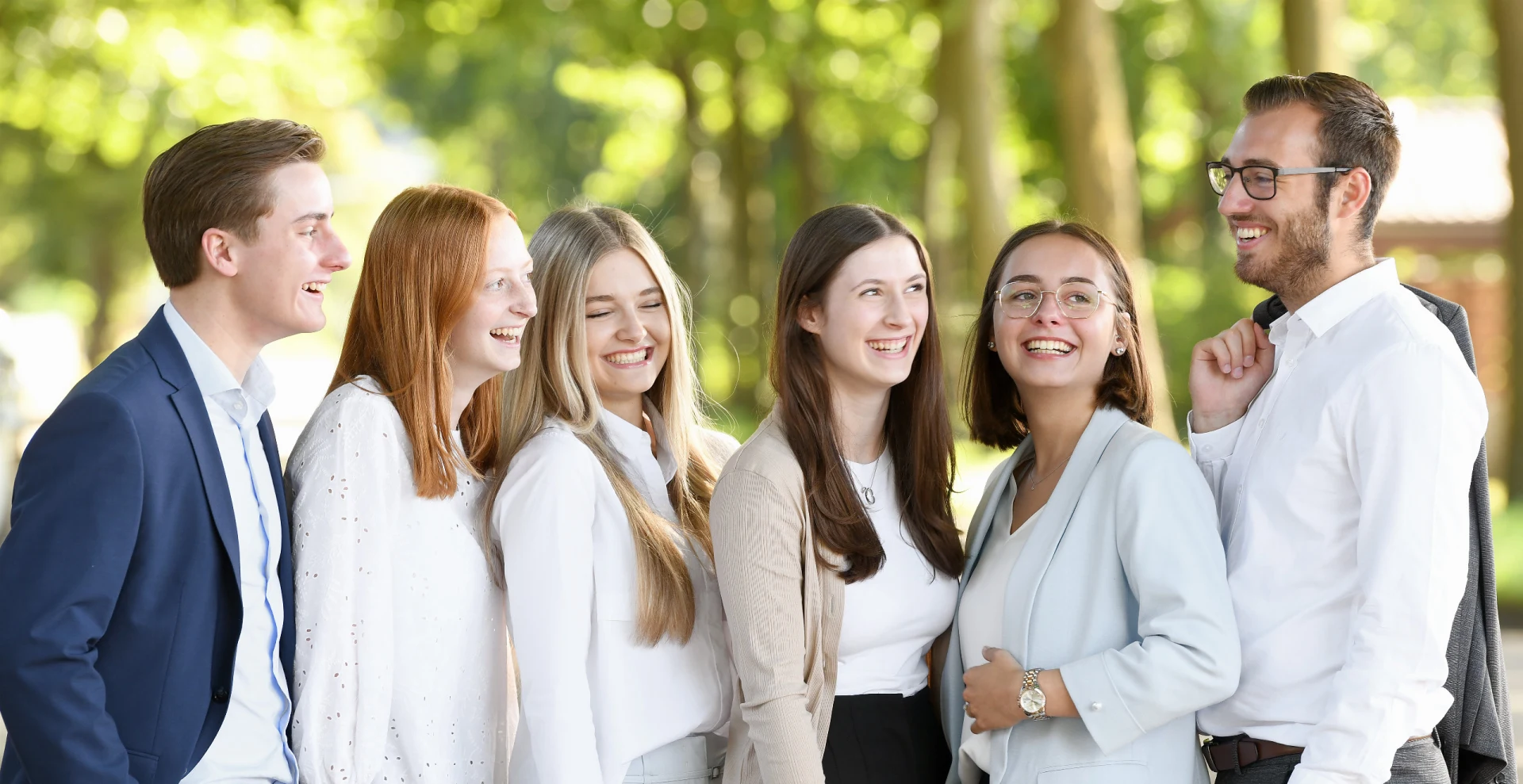 sechs junge Azubis stehen lachend für ein Gruppenfoto in einer Reihe