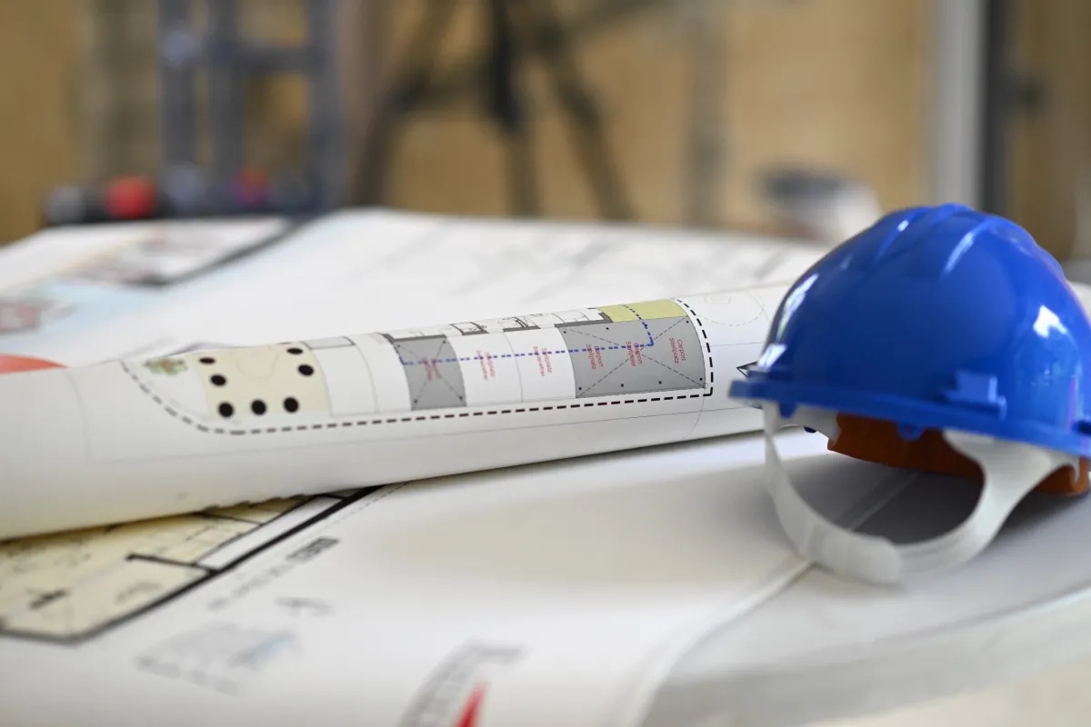 Auf einem Bauplan liegt ein blauer Helm