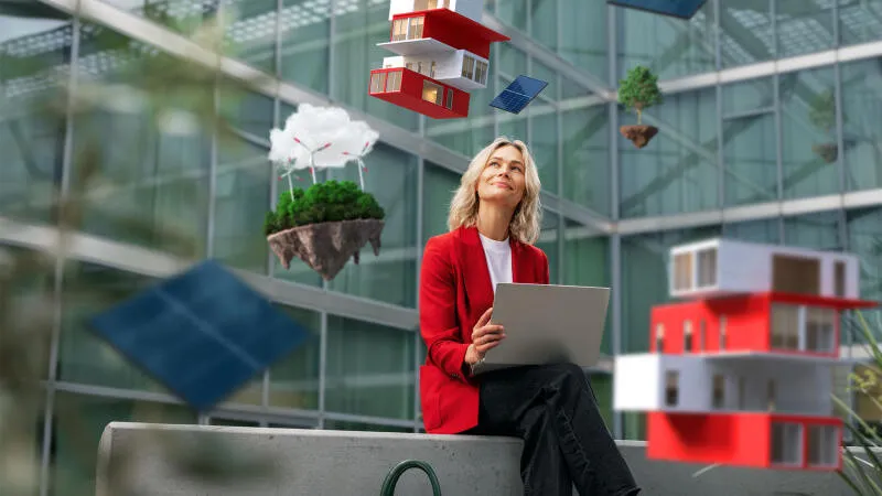 Eine Frau sitzt lächelnd in einem Innenhof. Um sie herum fliegen Häuser, Photovoltaikanlagen und Bäume. 