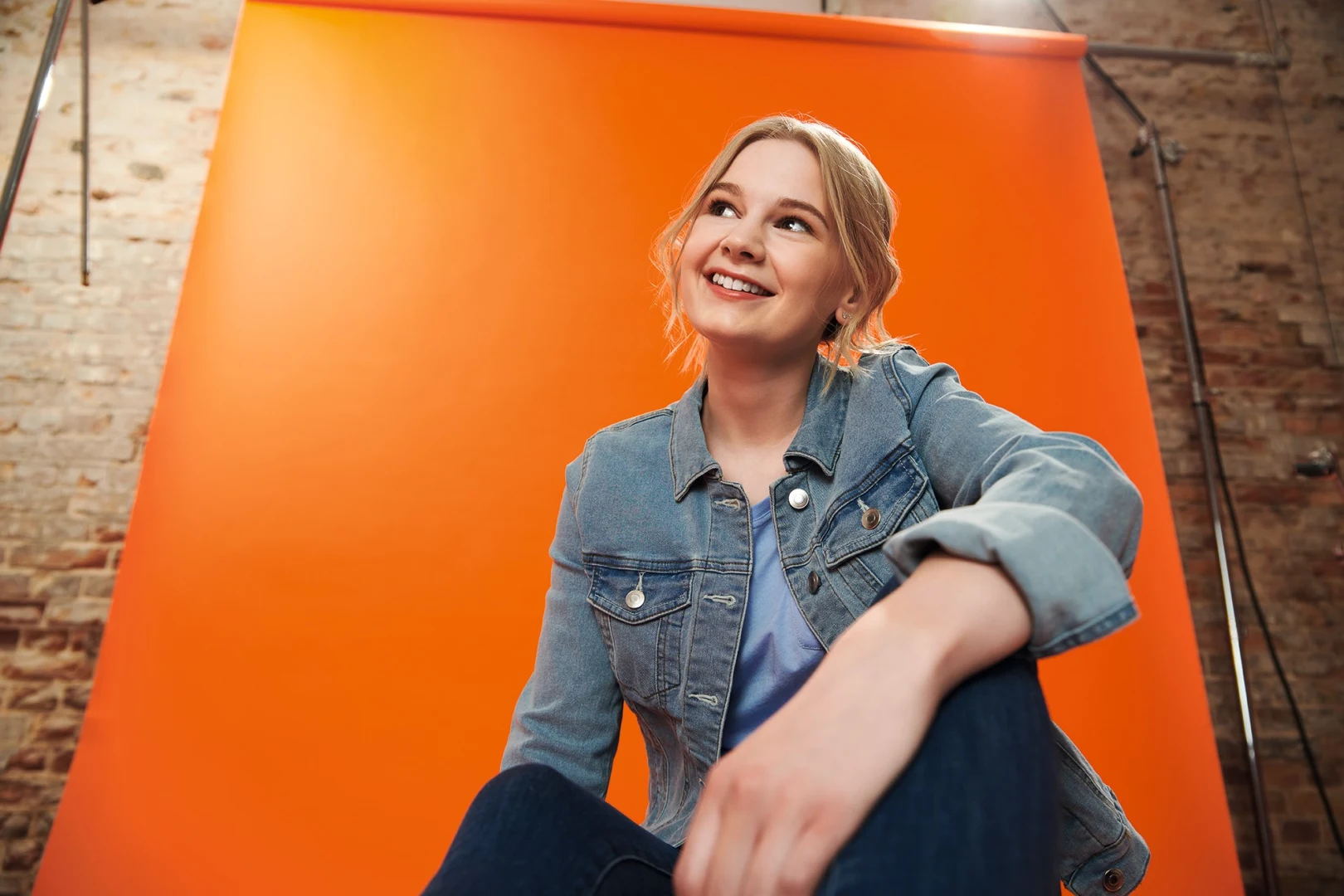 sitzendes Mädchen in Jeansjacke vor orangenem Hintergrund