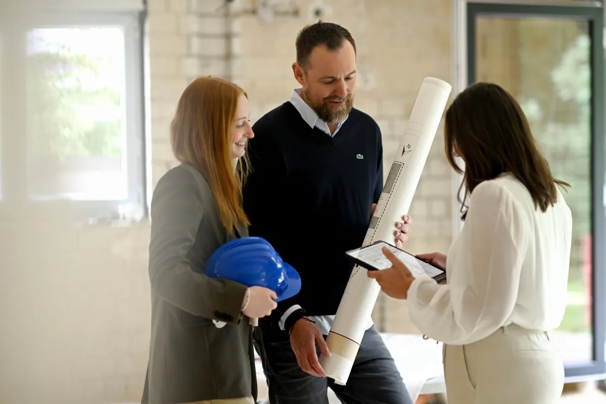 drei Personen auf Baustelle mit Plänen in der Hand